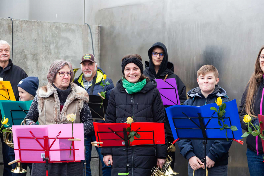 Bläserinnen und Bläser unterschiedlichen Alters stehen mit Instrumenten vor Notenständern an der Hinterlandmauer und lächeln in die Kamera.